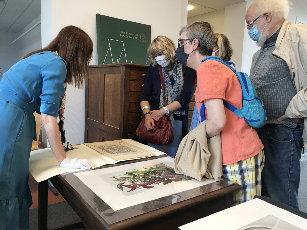 Agrandir l'image - fenêtre modale - Plusieurs personnes, dont une professeure et des visiteurs, se penchent sur un plan d'archive posé sur une table et présenté lors des Journées européeennes du patrimoine 2021.