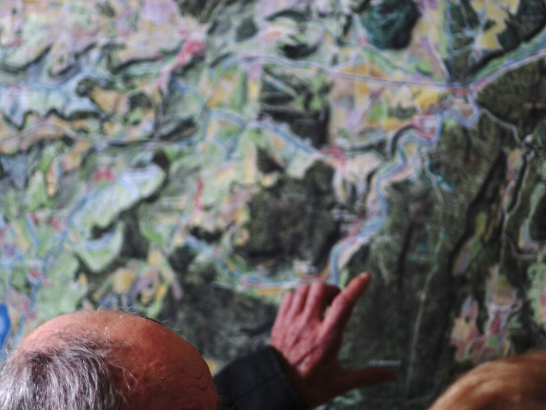 Agrandir l'image - fenêtre modale - Un habitant pointe du doight un élément sur la carte paysagère accrochée au mur.