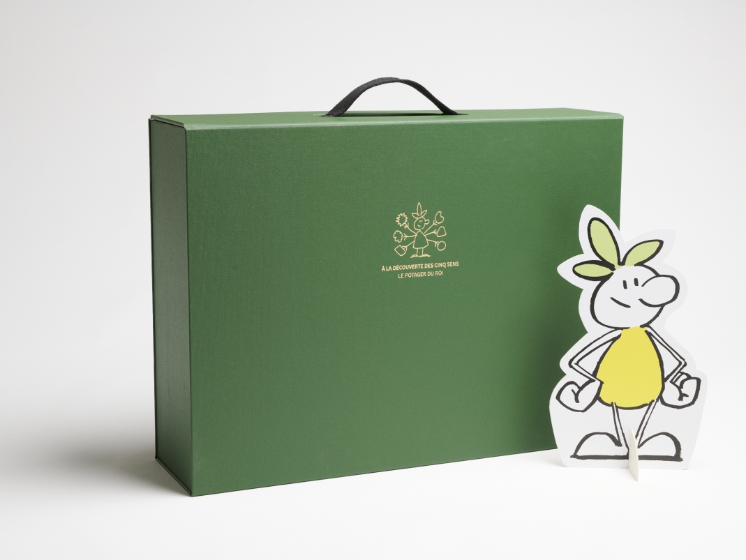 Agrandir l'image - fenêtre modale - Vue de la mallette pédagogique du Potager du Roi fermée avec la mascotte Trifoli posée devant elle, sur fond blanc.